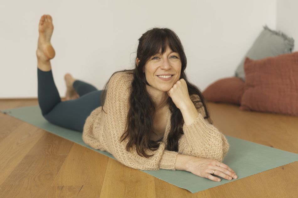 Isabella Börner, liegt bäuchlings auf Yogamatte und stützt Kopf auf Hand.